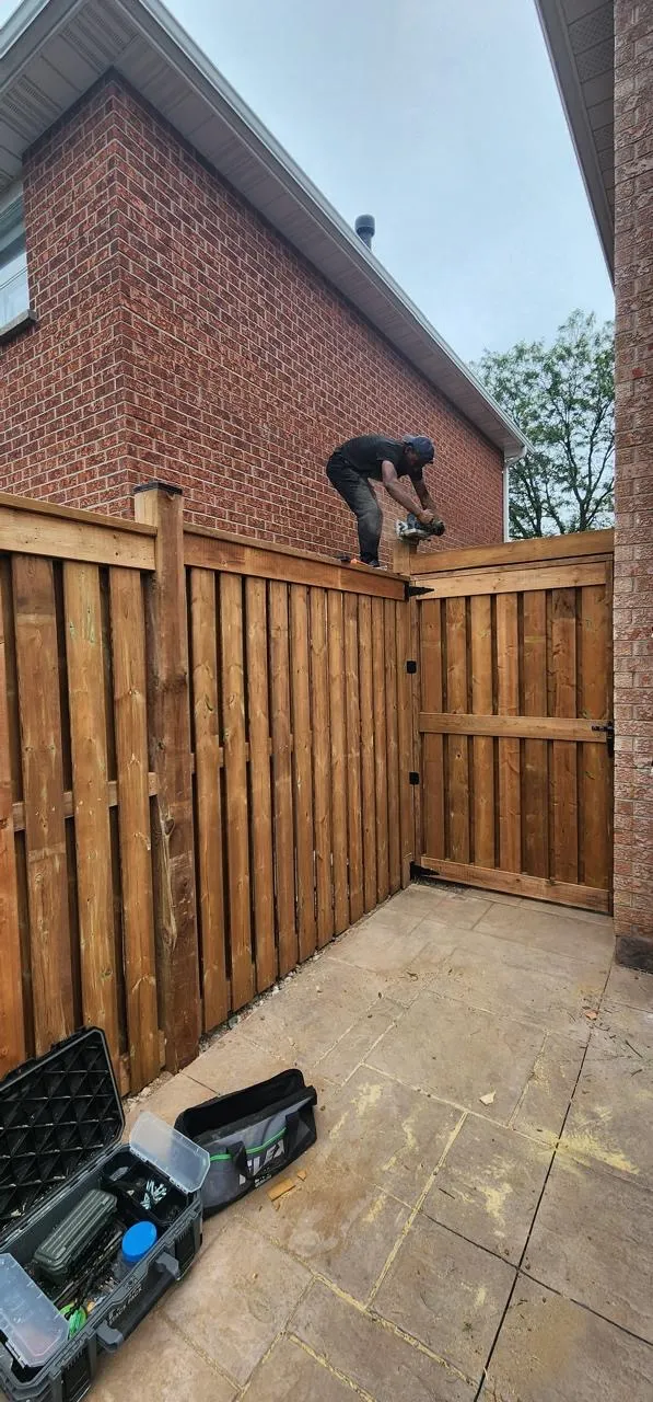 Installer fastening the top rail of a cedar fence and gate