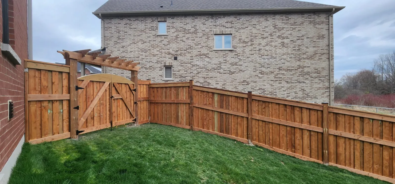 Finished cedar fence with an arbor gate beside a brick home